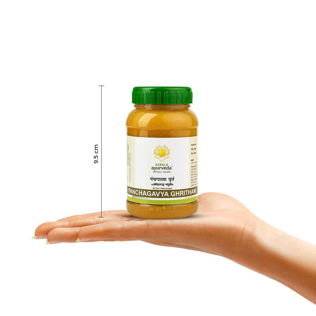  A hand holding a jar of Kerala Ayurveda Panchagavya Ghritham, with a measurement indicator showing its height as 9.5 cm. The product name and brand logo are visible on the label. – Kerala Ayurveda India