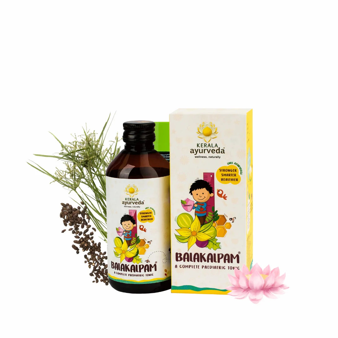 Clean product shot of Kerala Ayurveda Balakalpam pediatric tonic bottle with matching carton, lotus flower and medicinal herbs arranged around it – Kerala Ayurveda India